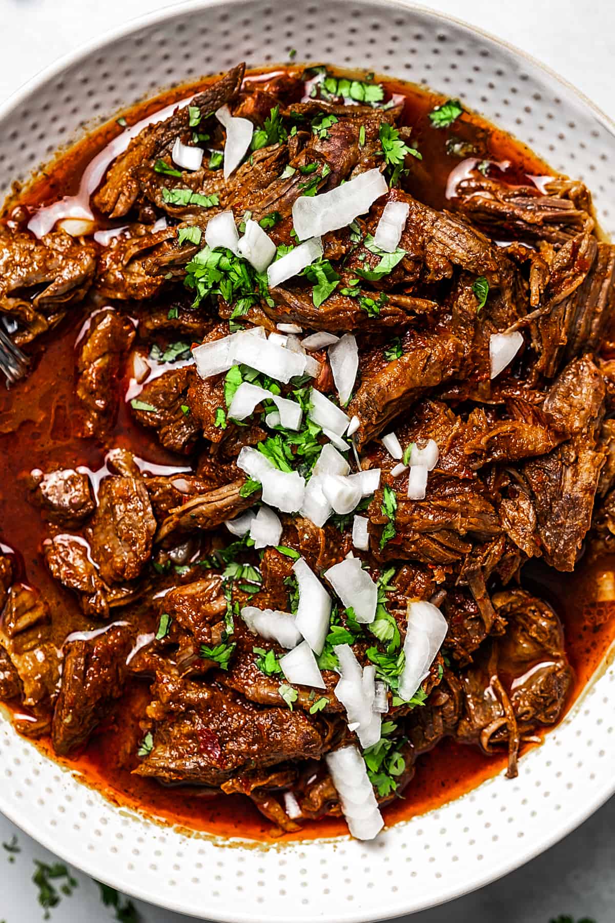 Close up shot of spicy shredded beef with tortillas and garnishes.