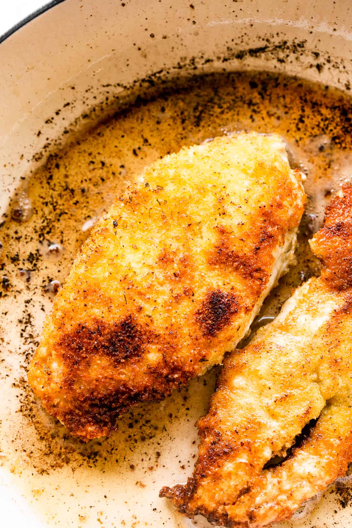 breaded chicken frying in a white pan.