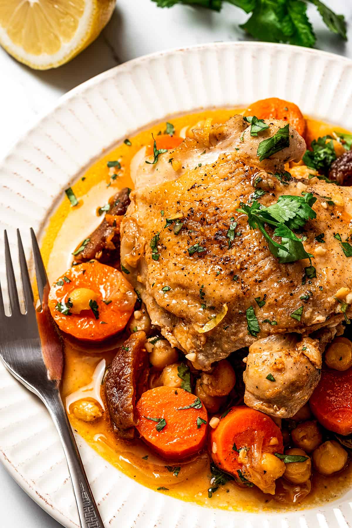 A plate of chicken thighs cooked in Moroccan tagine sauce with vegetables.
