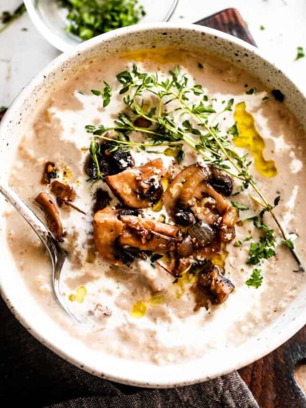 overhead photo of a bowl with creamy mushroom soup, garnished with mushrooms, greens, and a swirl of heavy cream.