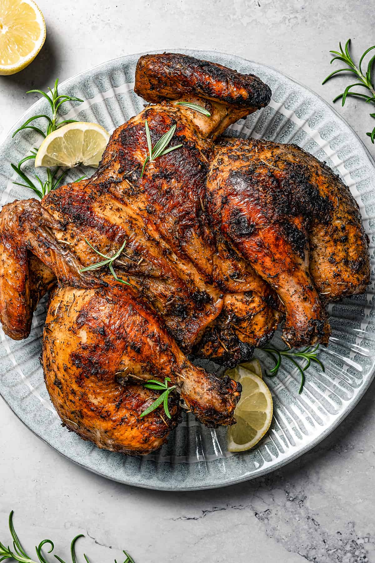 Spatchcock grilled chicken garnished with rosemary and lemon.