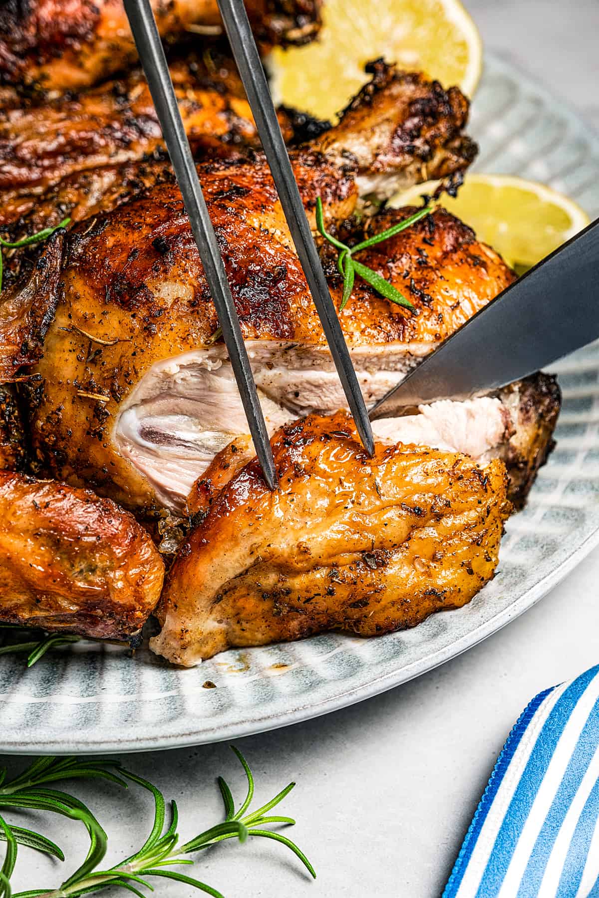 Slicing into a grilled whole chicken with a knife and carving fork.