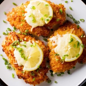 overhead shot of three breaded chicken breasts, also known as chicken milanese, arranged on a plate and topped with lemon slices.