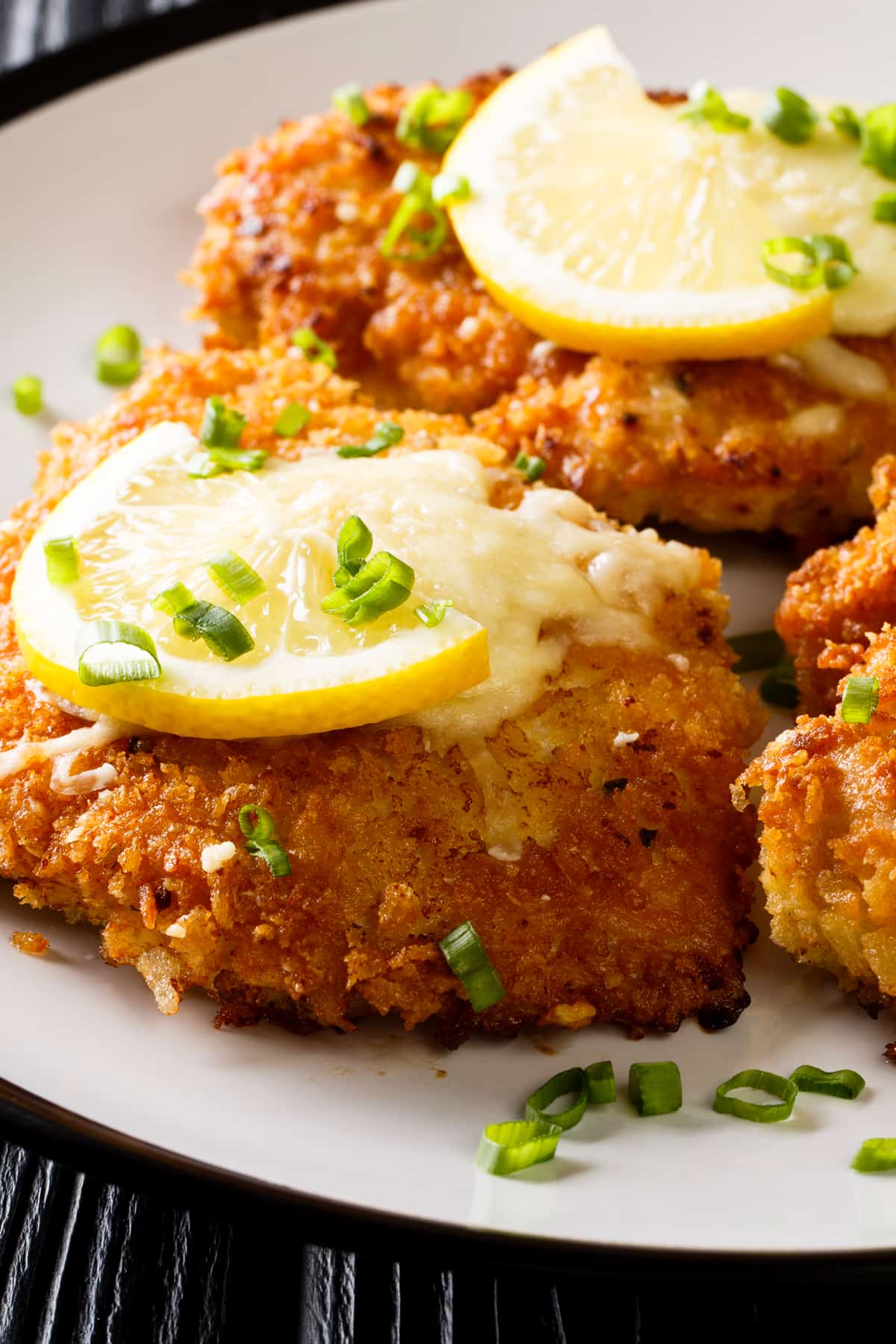 up close shot of breaded chicken breasts arranged on a plate and topped with lemon slices.
