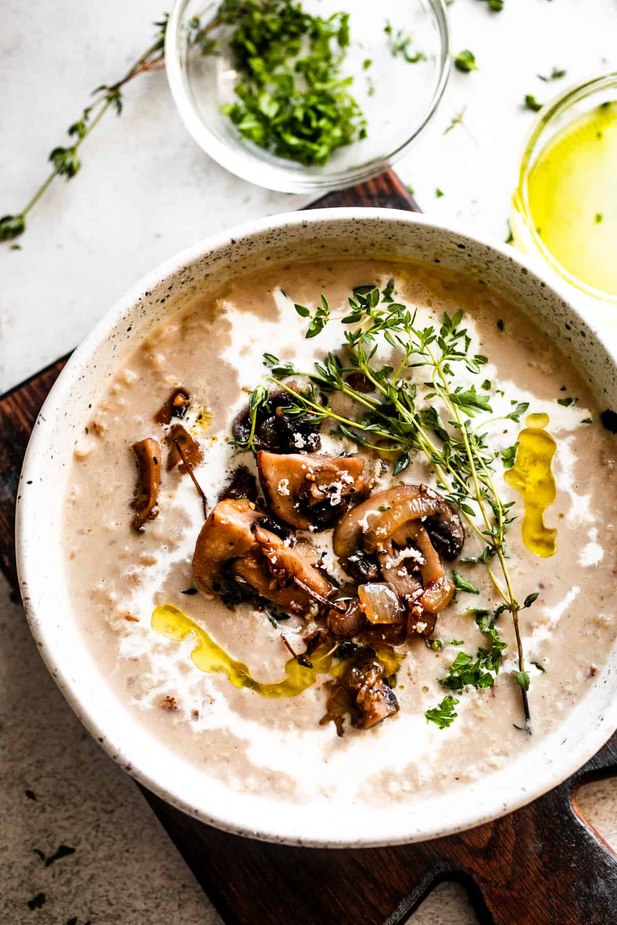 overhead photo of a bowl with creamy mushroom soup, garnished with mushrooms, greens, and a swirl of heavy cream.