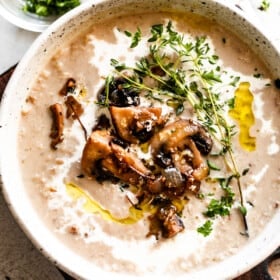 overhead photo of creamy mushroom soup and rice in a bowl garnished with whole mushrooms, greens, and a swirl of heavy cream.