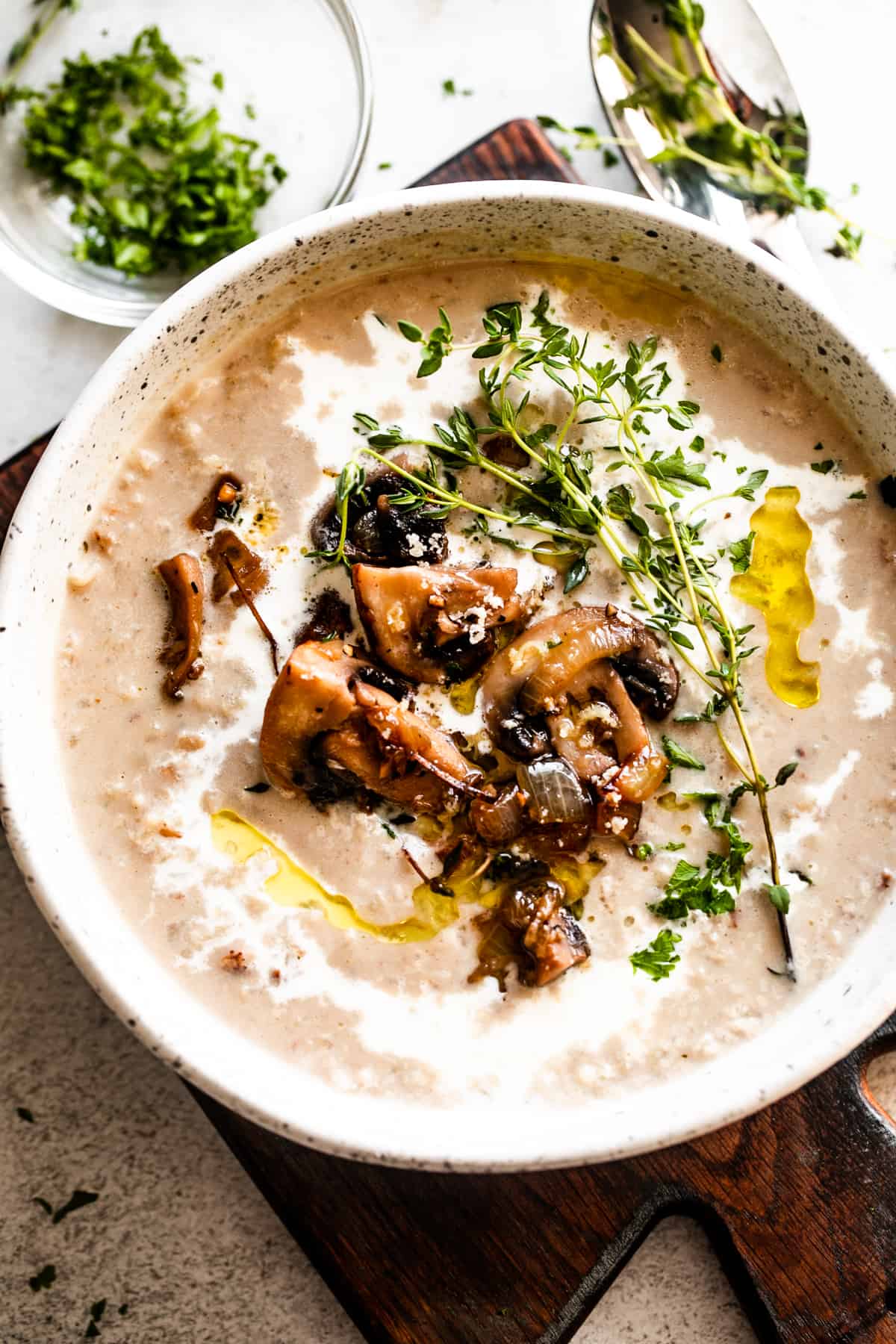 overhead photo of creamy mushroom soup and rice in a bowl garnished with whole mushrooms, greens, and a swirl of heavy cream.