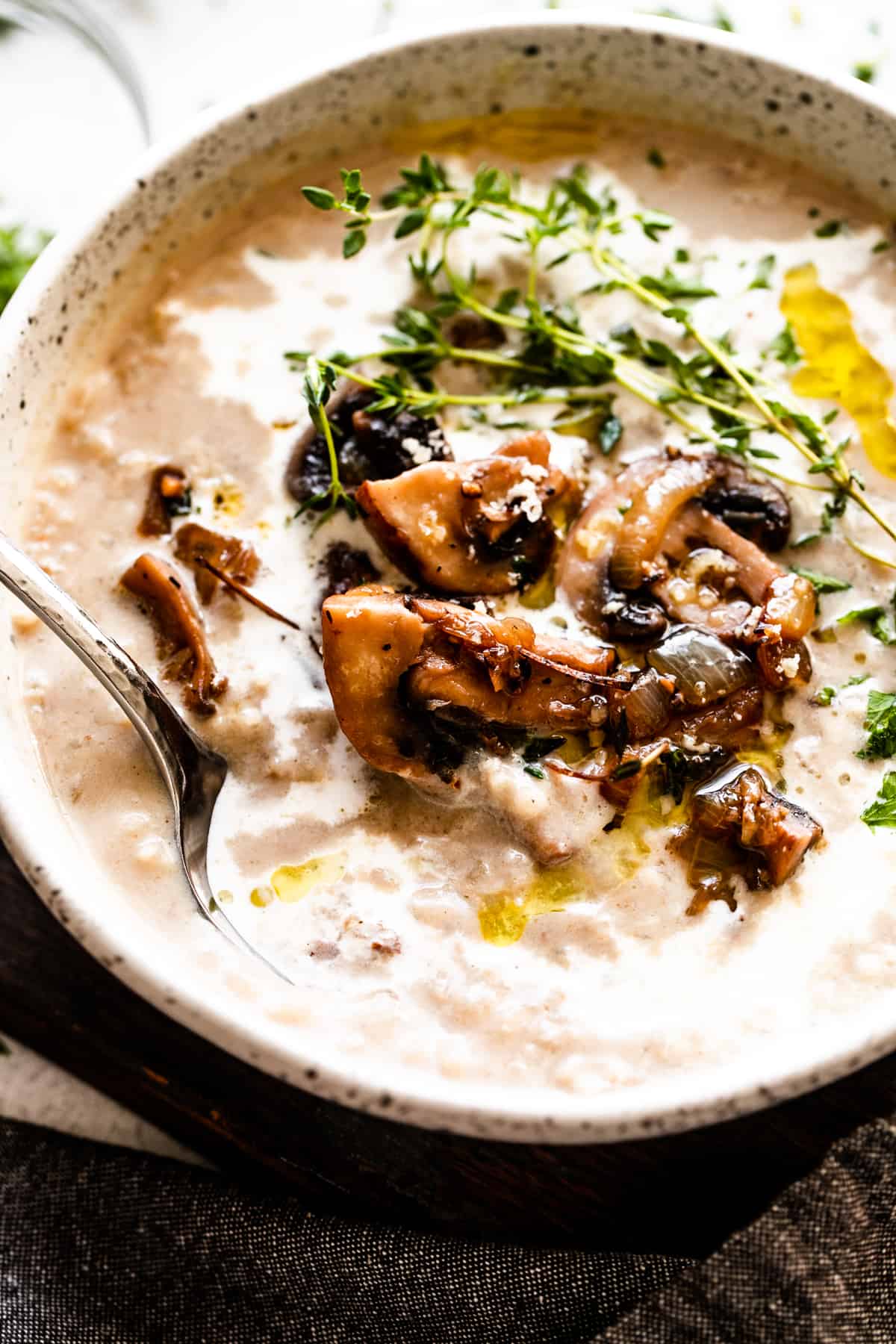 photo of a bowl with creamy mushroom soup, garnished with mushrooms, greens, and a swirl of heavy cream.