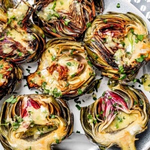 overhead shot of a serving plate with baked artichokes drizzled with lemon dressing.