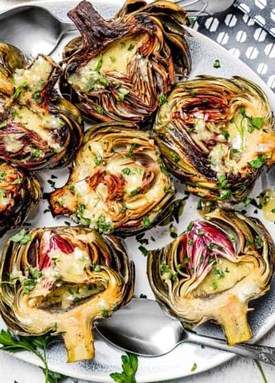 overhead shot of a serving plate with baked artichokes drizzled with lemon dressing.