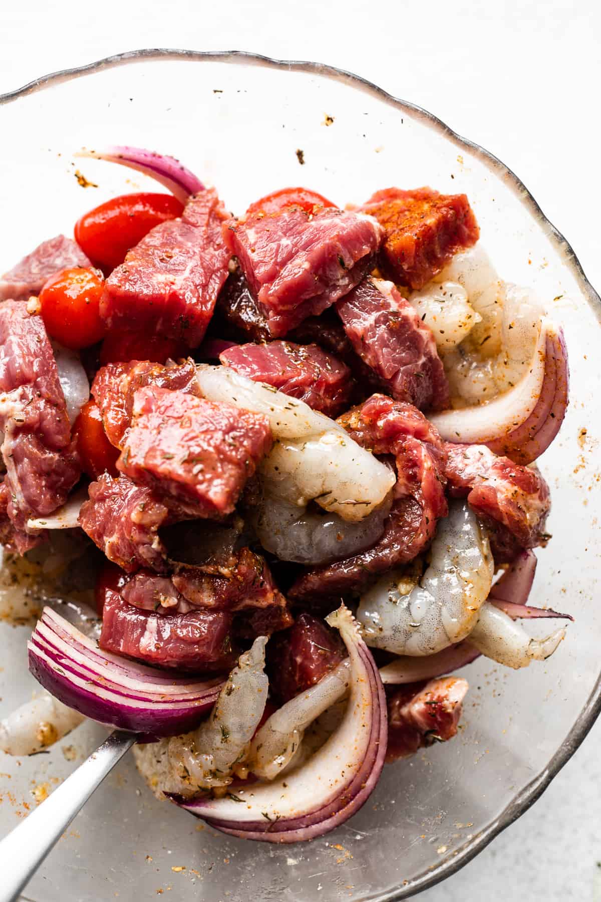 raw steak cubes, raw shrimp, and red onions, in a glass bowl.