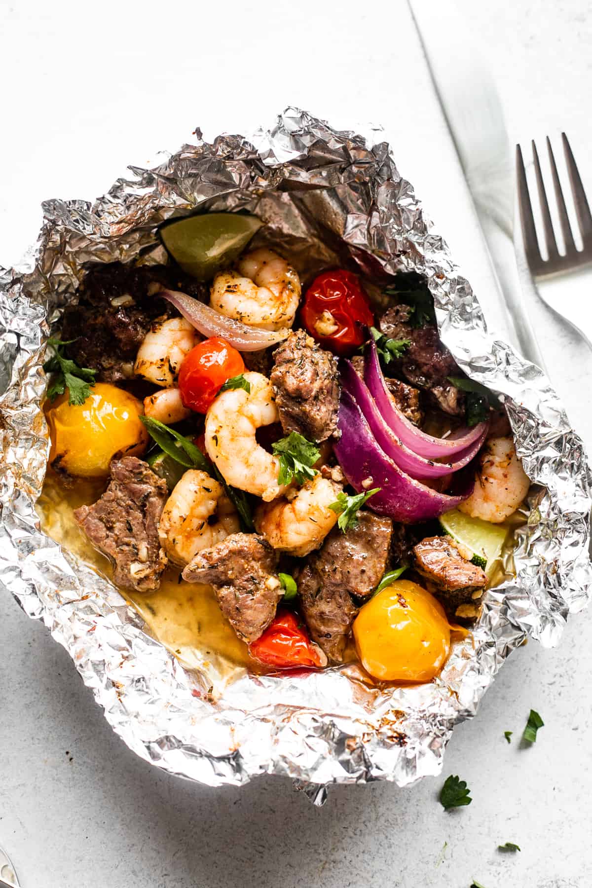 overhead shot of surf and turf foil pack filled with steak bites, shrimp, red onions, and colored grape tomatoes.