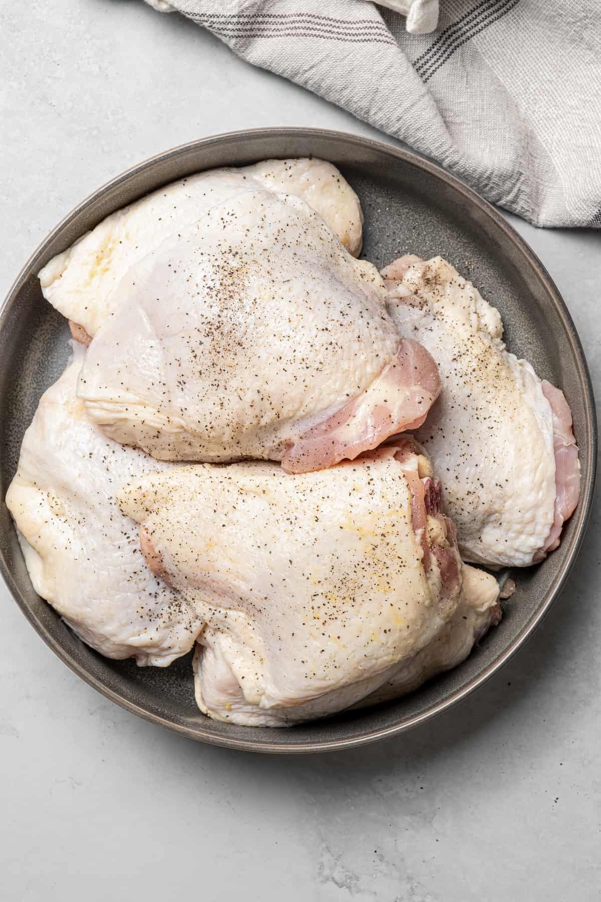 Bone-in skin-on chicken thighs sprinkled with seasonings.