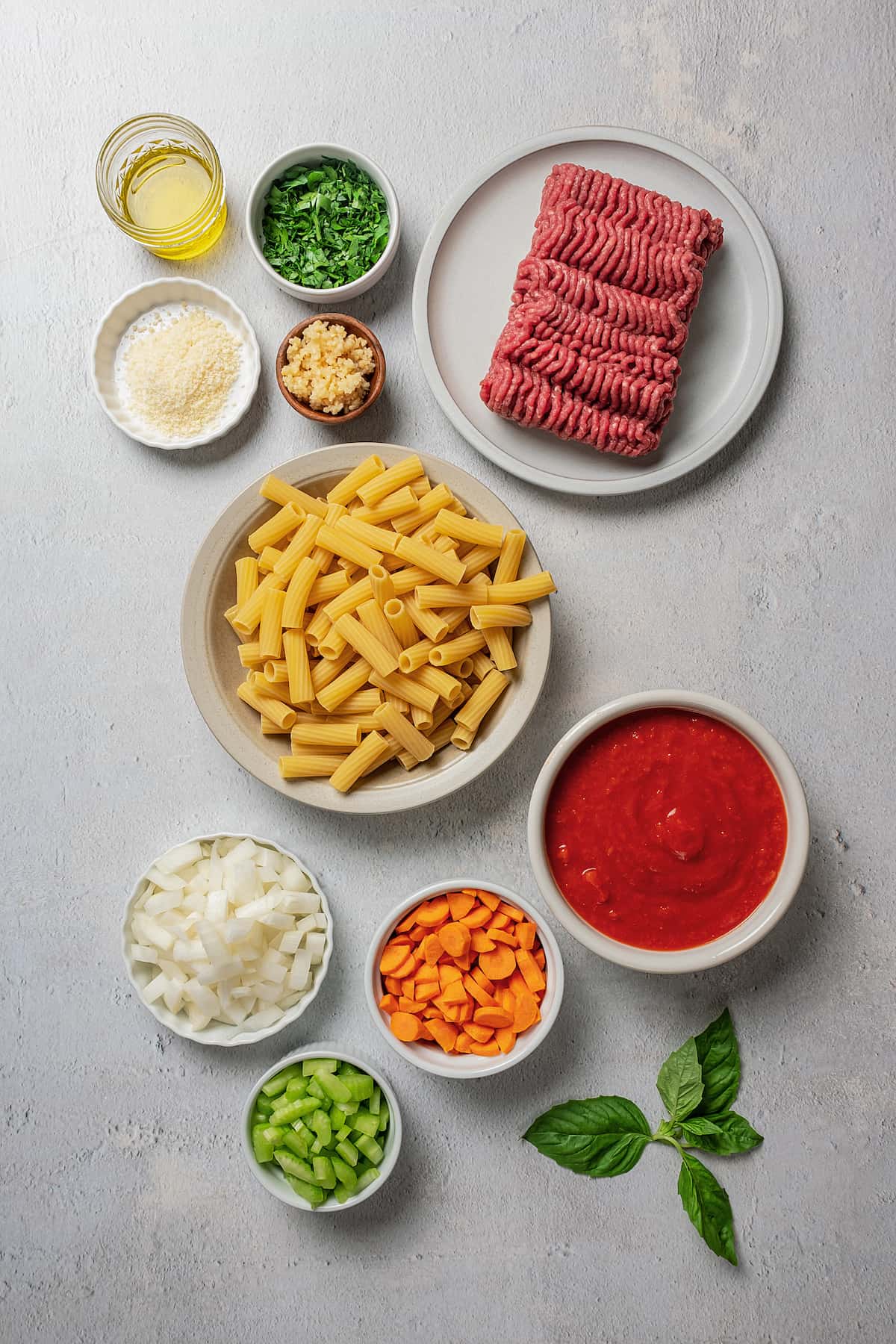 From top: olive oil, chopped herbs, ground beef, parmesan cheese, garlic, pasta, diced onion, carrots, tomato sauce, celery.