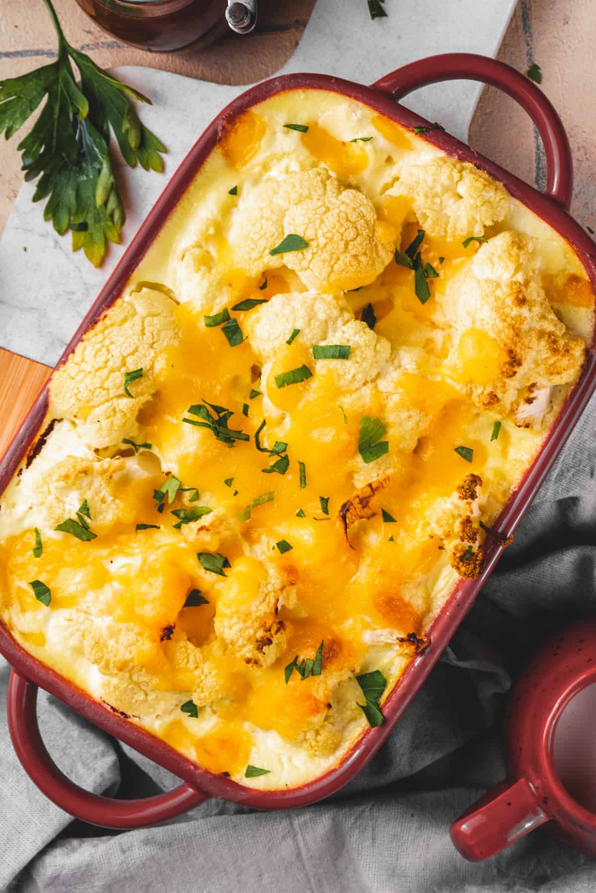 dark red baking dish with a loaded cheesy cauliflower casserole in creamy sauce.