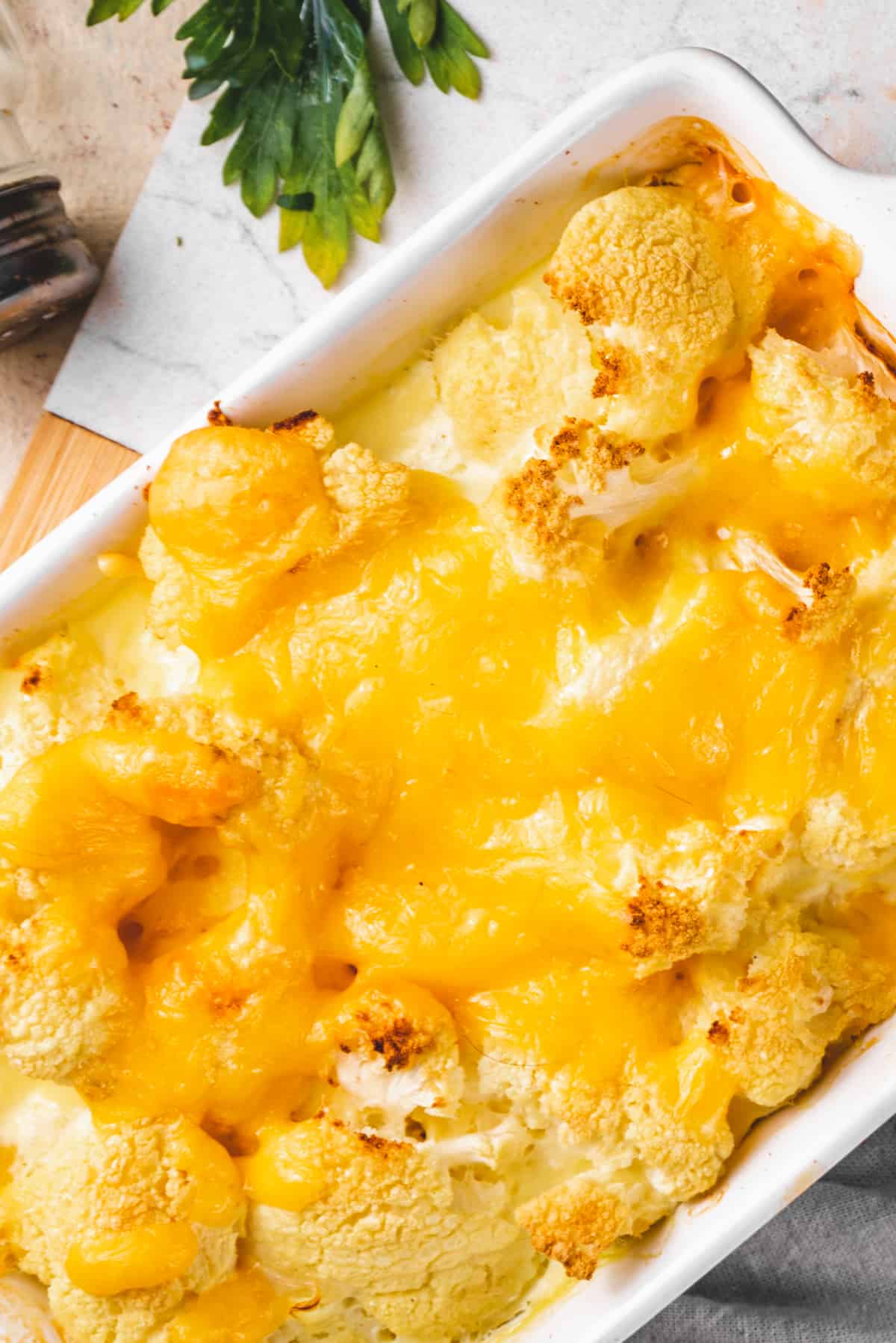 close up shot of a baking dish with a loaded cheesy cauliflower casserole in creamy sauce.