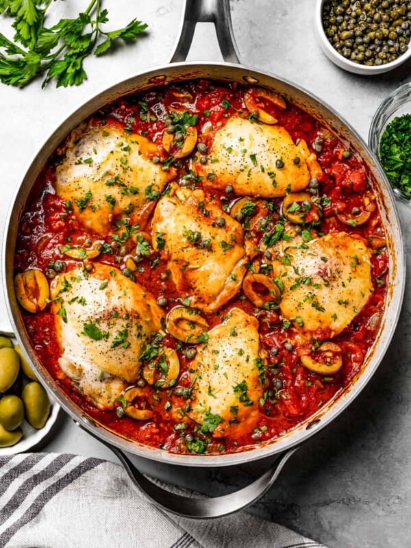 A deep skillet of chicken puttanesca with bone-in thighs and herbs.