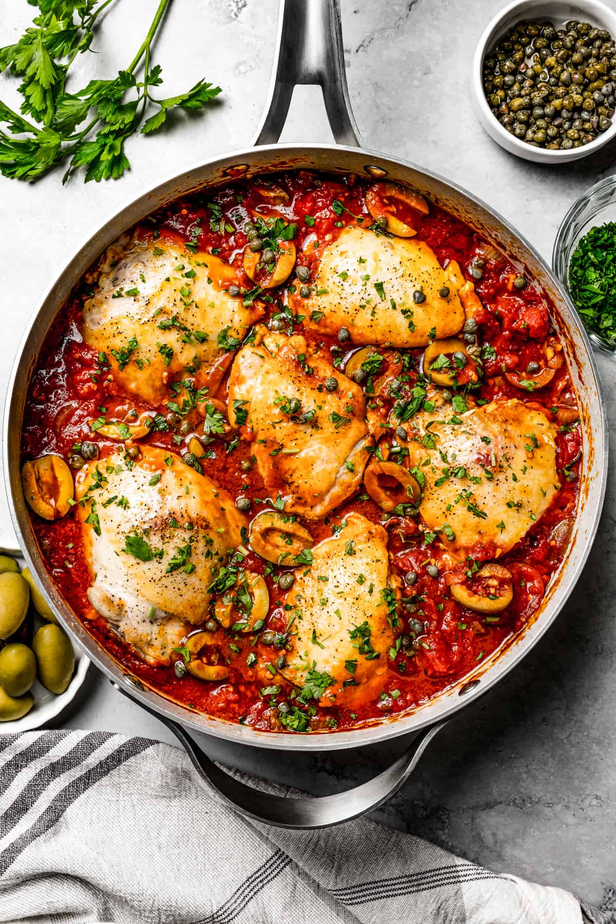 A deep skillet of chicken puttanesca with bone-in thighs and herbs.