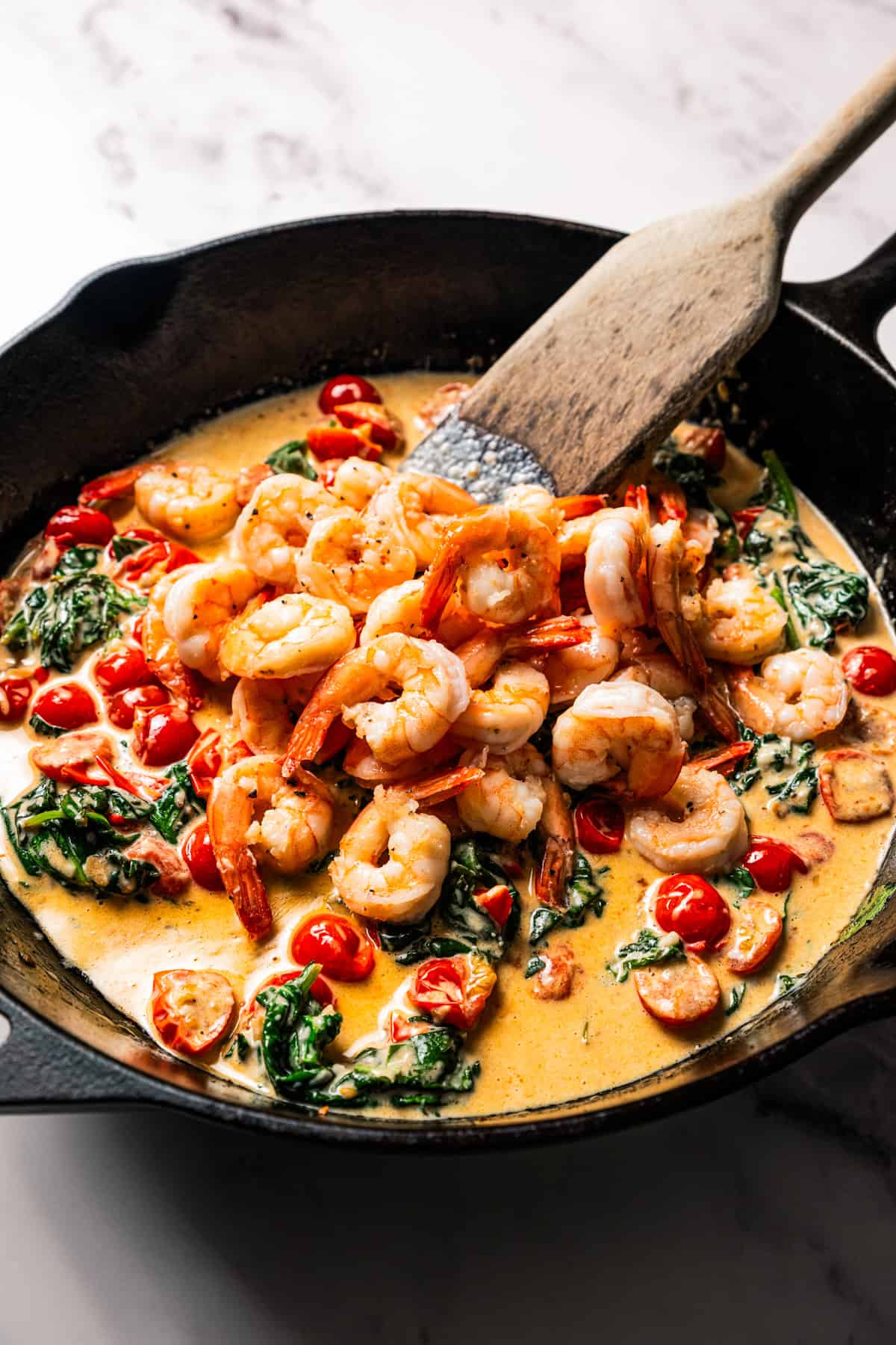 Stirring shrimp through a cream sauce in a skillet.