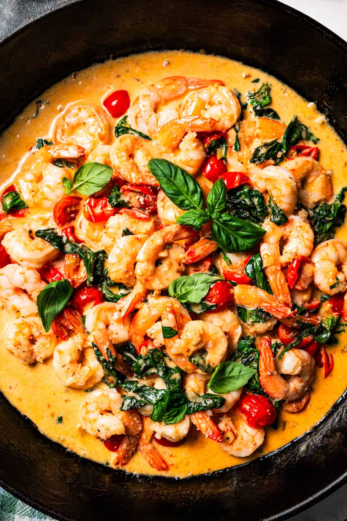 Close-up shot of creamy shrimp with spinach and tomatoes in a skillet.