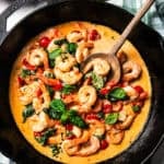 A skillet of cooked shrimp, tomatoes, and spinach in cream sauce.