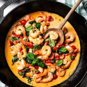 A skillet of cooked shrimp, tomatoes, and spinach in cream sauce.