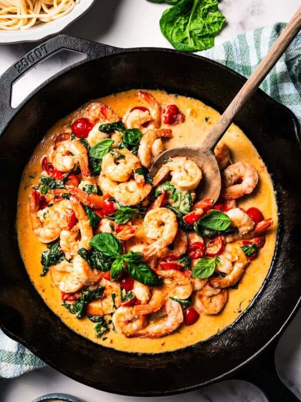A skillet of cooked shrimp, tomatoes, and spinach in cream sauce.