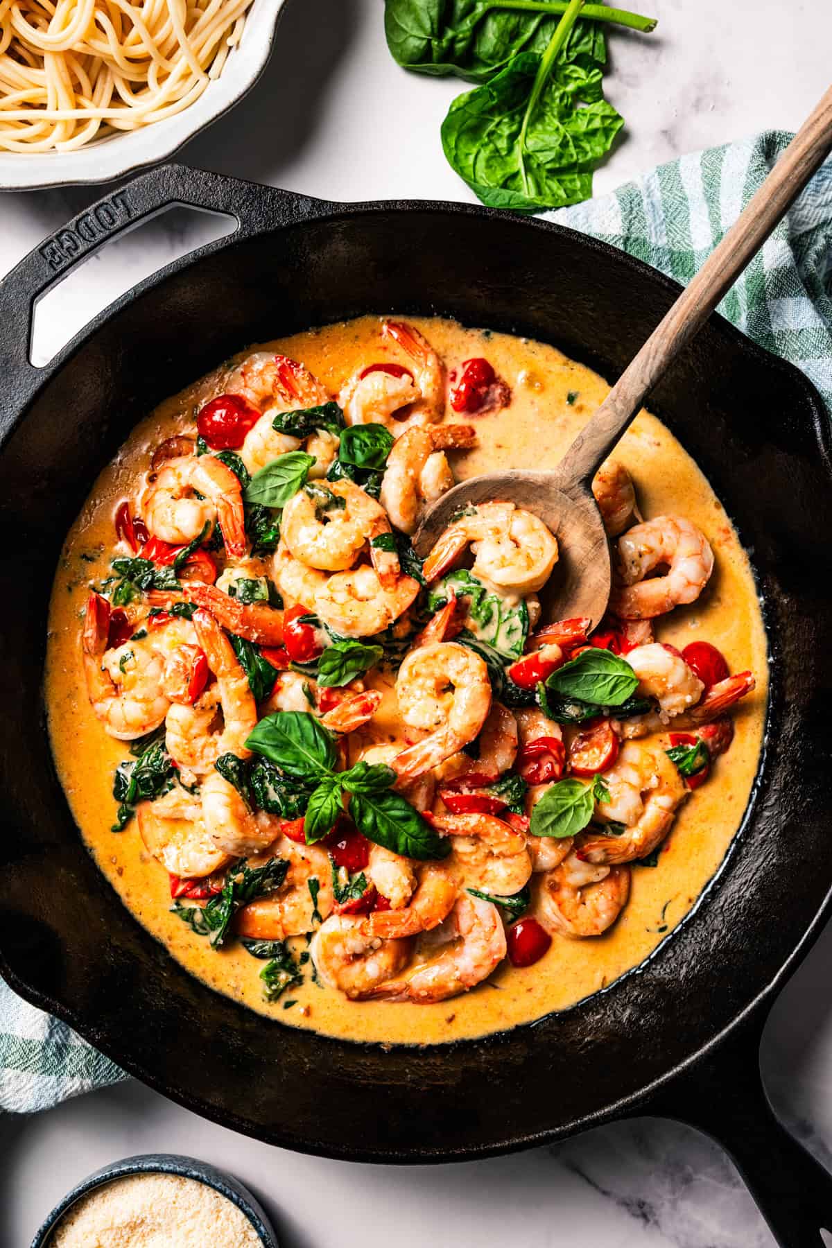 A skillet of cooked shrimp, tomatoes, and spinach in cream sauce.