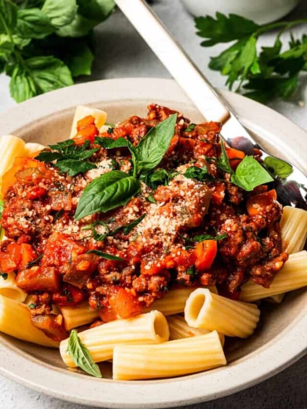A shallow bowl with pasta an meat sauce, topped with sprigs of fresh basil.
