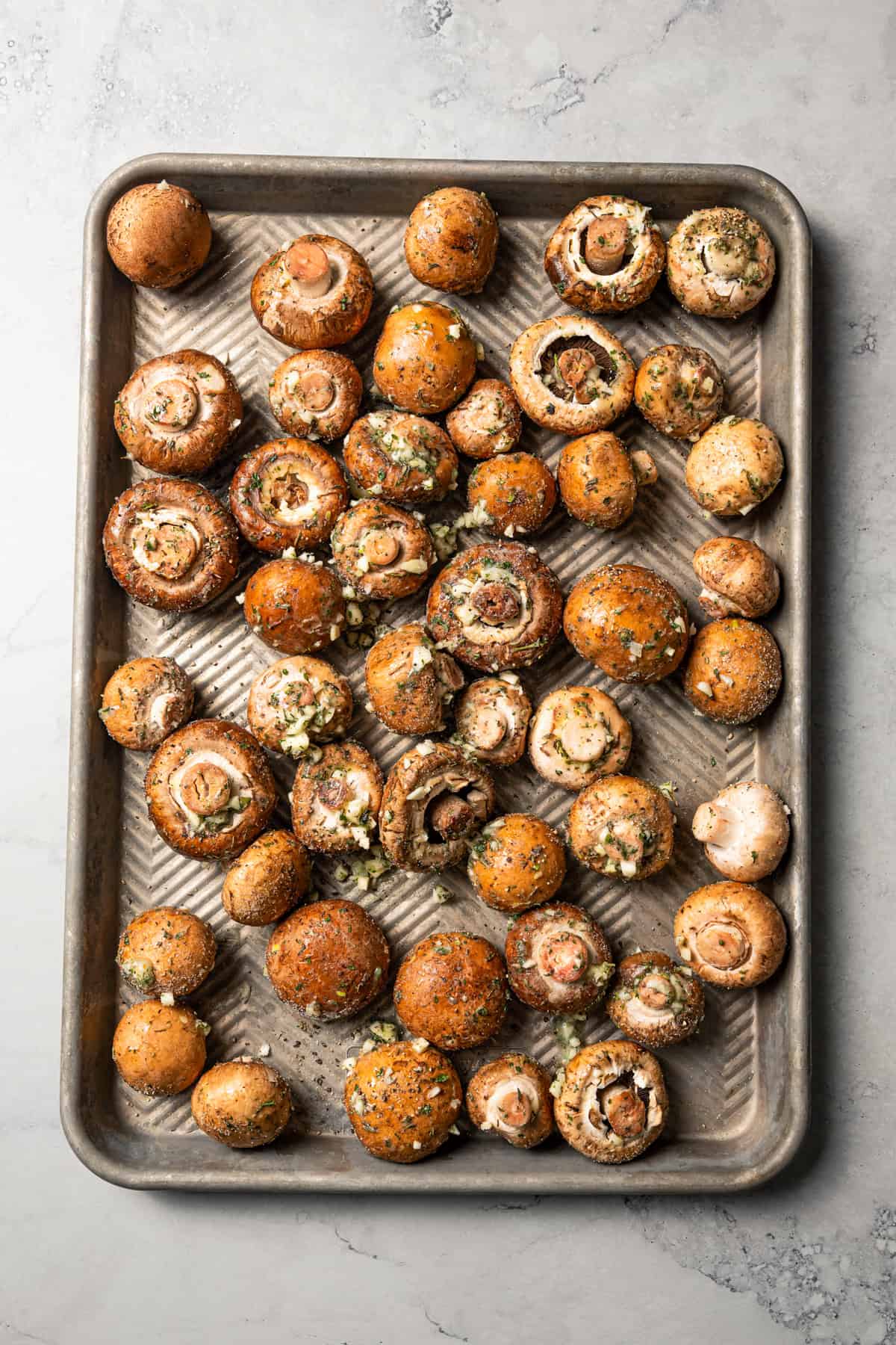 This roasted mushroom recipe combines buttery cremini mushrooms with garlic and herbs. It's a quick, easy side dish with only 5 ingredients! Brown mushrooms on a baking sheet.