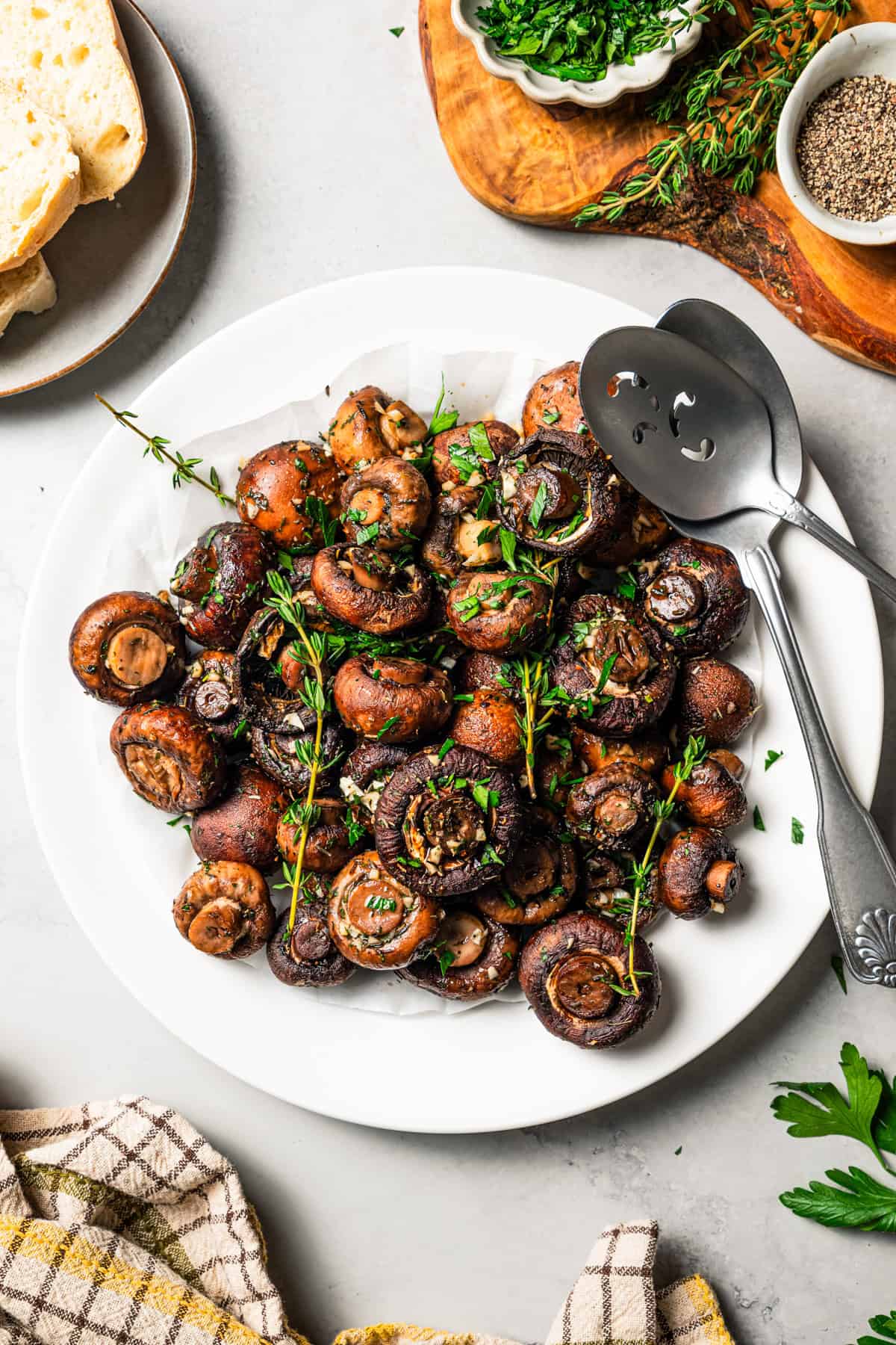 This roasted mushroom recipe combines buttery cremini mushrooms with garlic and herbs. It's a quick, easy side dish with only 5 ingredients! Overhead view of roasted mushrooms garnished with fresh thyme sprigs on a white plate with two serving spoons.