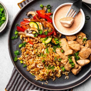 Hibachi chicken, yum yum sauce, sauteed veggies and fried rice with a fork holding a bite full of food