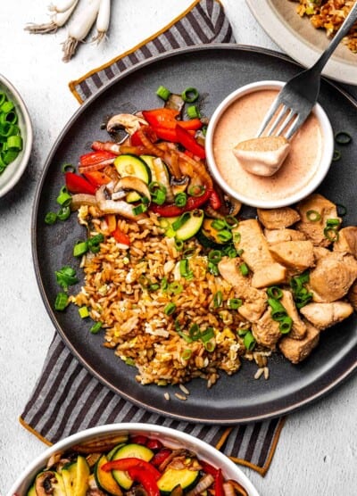 Hibachi chicken, yum yum sauce, sauteed veggies and fried rice with a fork holding a bite full of food