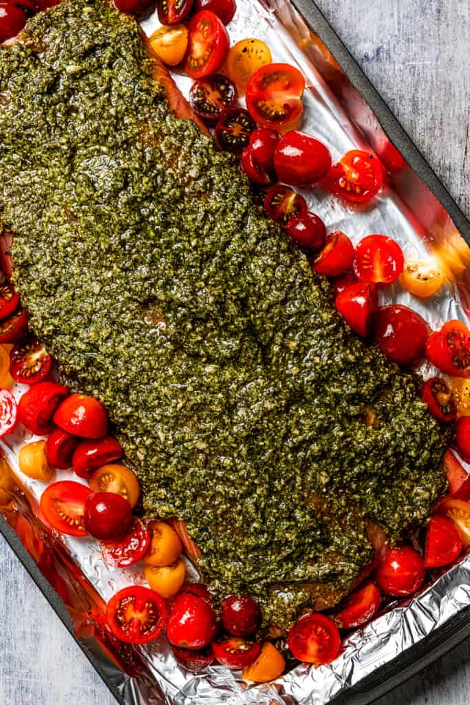A sheet pan with a pesto-covered salmon fillet surrounded by halved cherry tomatoes.
