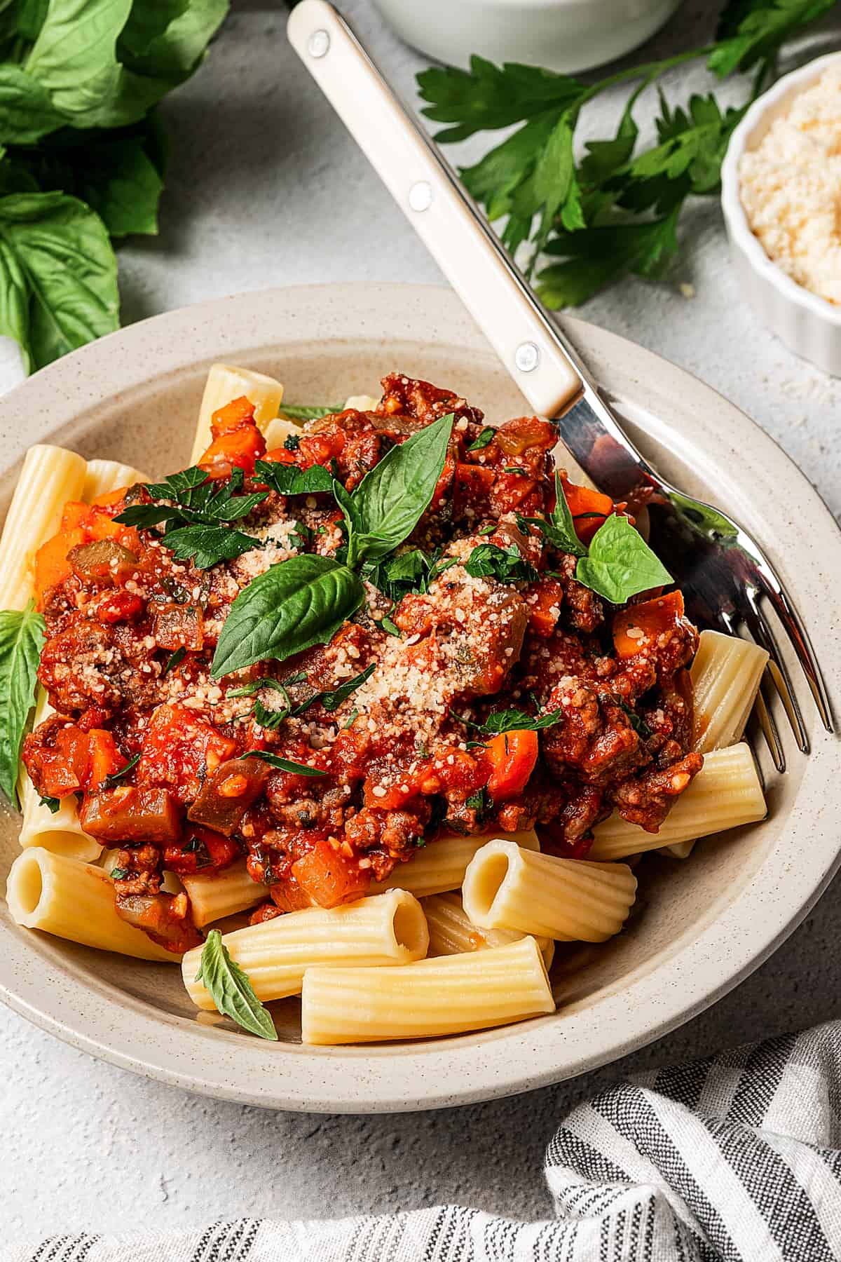 A shallow bowl with pasta an meat sauce, topped with sprigs of fresh basil.