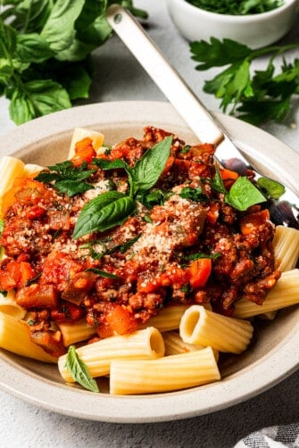A shallow bowl with pasta an meat sauce, topped with sprigs of fresh basil.