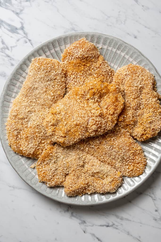 A plate of breaded raw chicken cutlets.