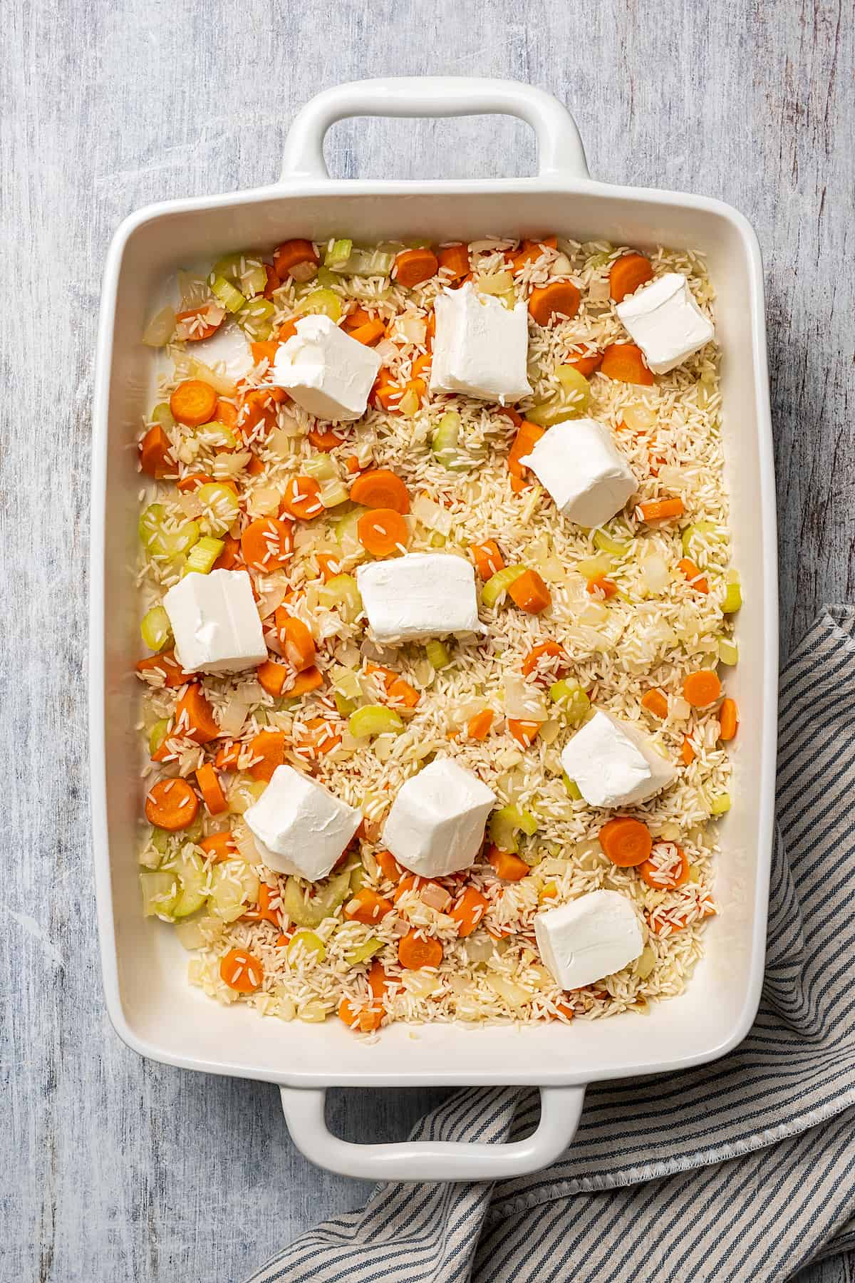 Cubed cream cheese dotted over a baking dish of rice and vegetables.