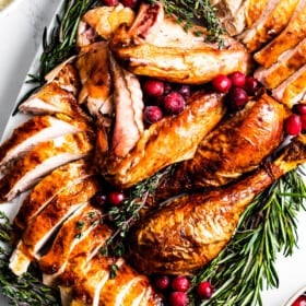 overhead shot of Sliced roasted turkey on a serving platter, surrounded with herbs and cranberries.