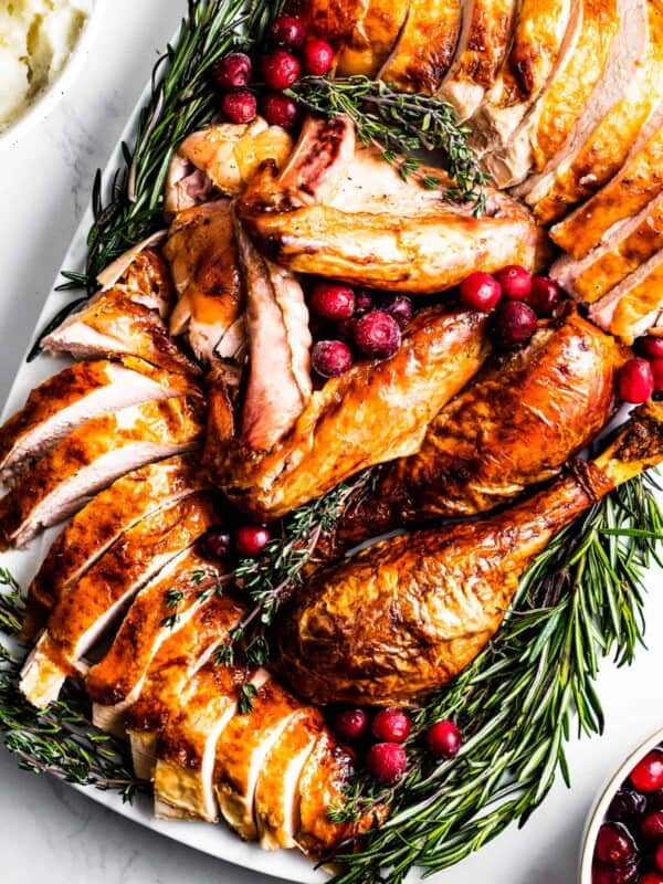 overhead shot of Sliced roasted turkey on a serving platter, surrounded with herbs and cranberries.