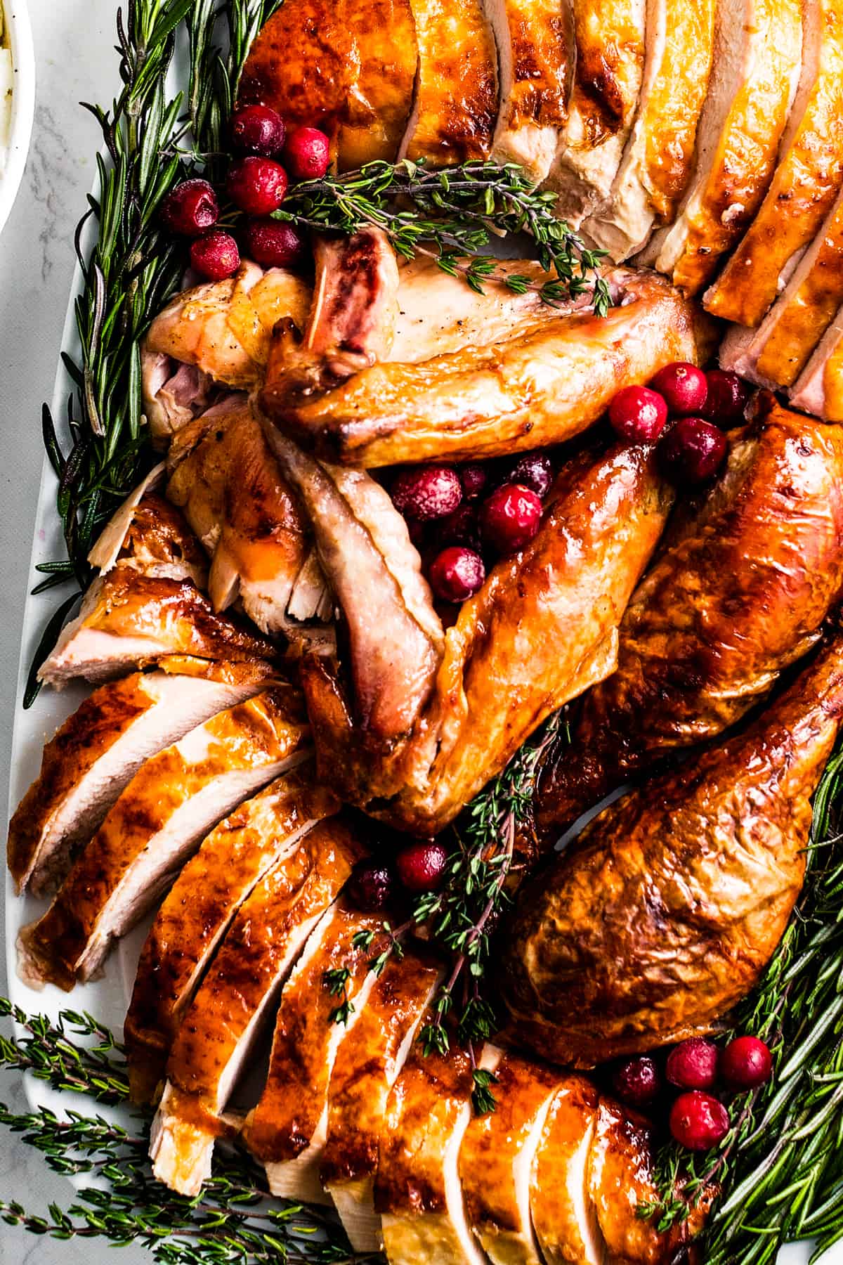 Sliced oven roasted turkey on a serving platter, surrounded with herbs and cranberries.