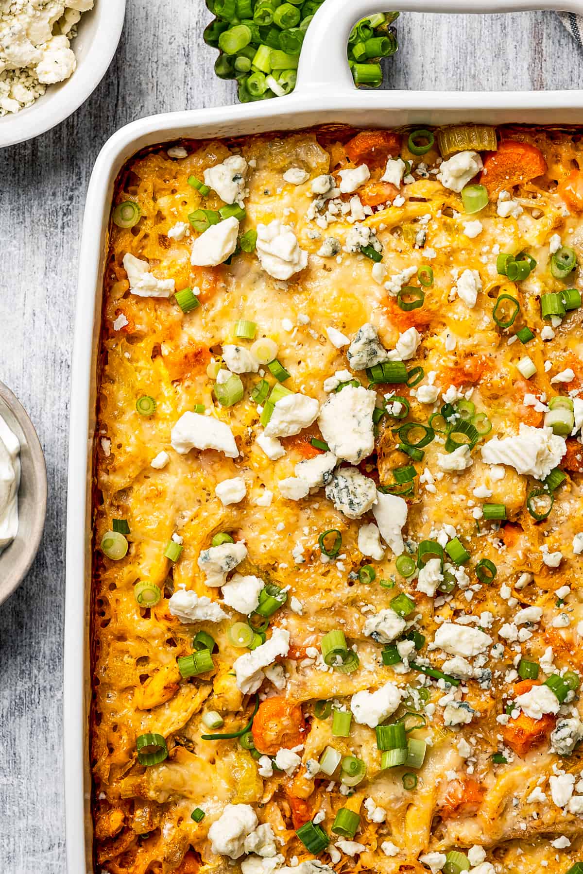 A cheesy casserole topped with blue cheese crumbles and sliced green onions.