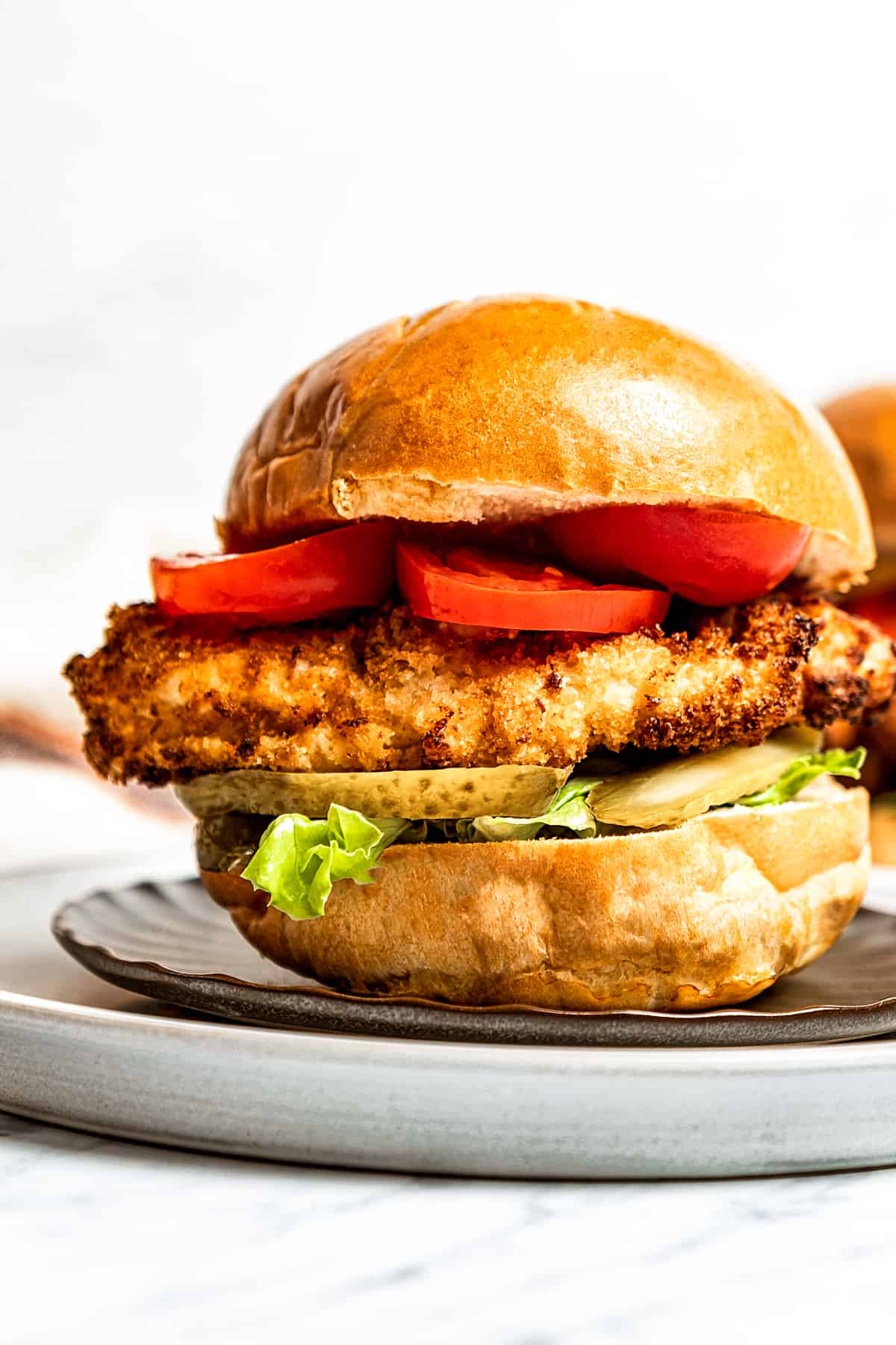 A fried chicken sandwich on a bun with lettuce, tomato, and pickles.