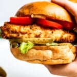 Holding a chicken sandwich toward the camera to show the air fryer chicken and toppings on a buttery bun.