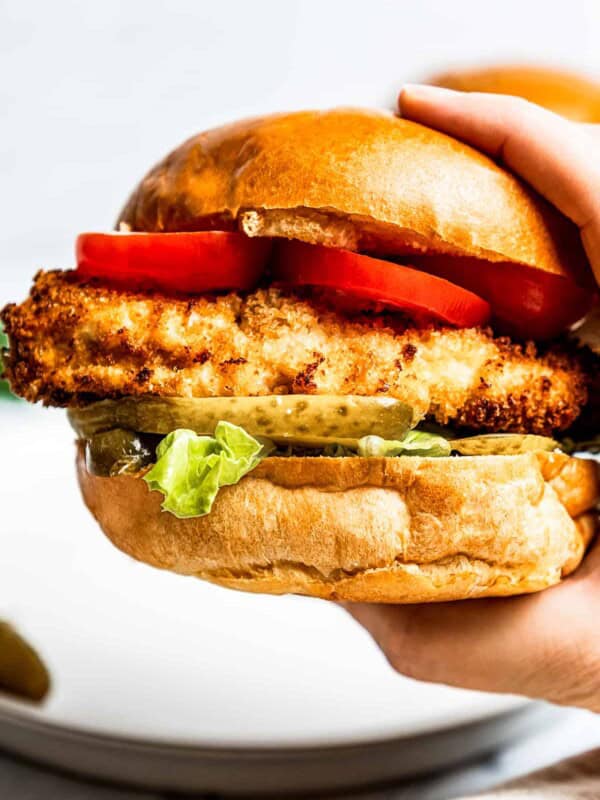 Holding a chicken sandwich toward the camera to show the air fryer chicken and toppings on a buttery bun.
