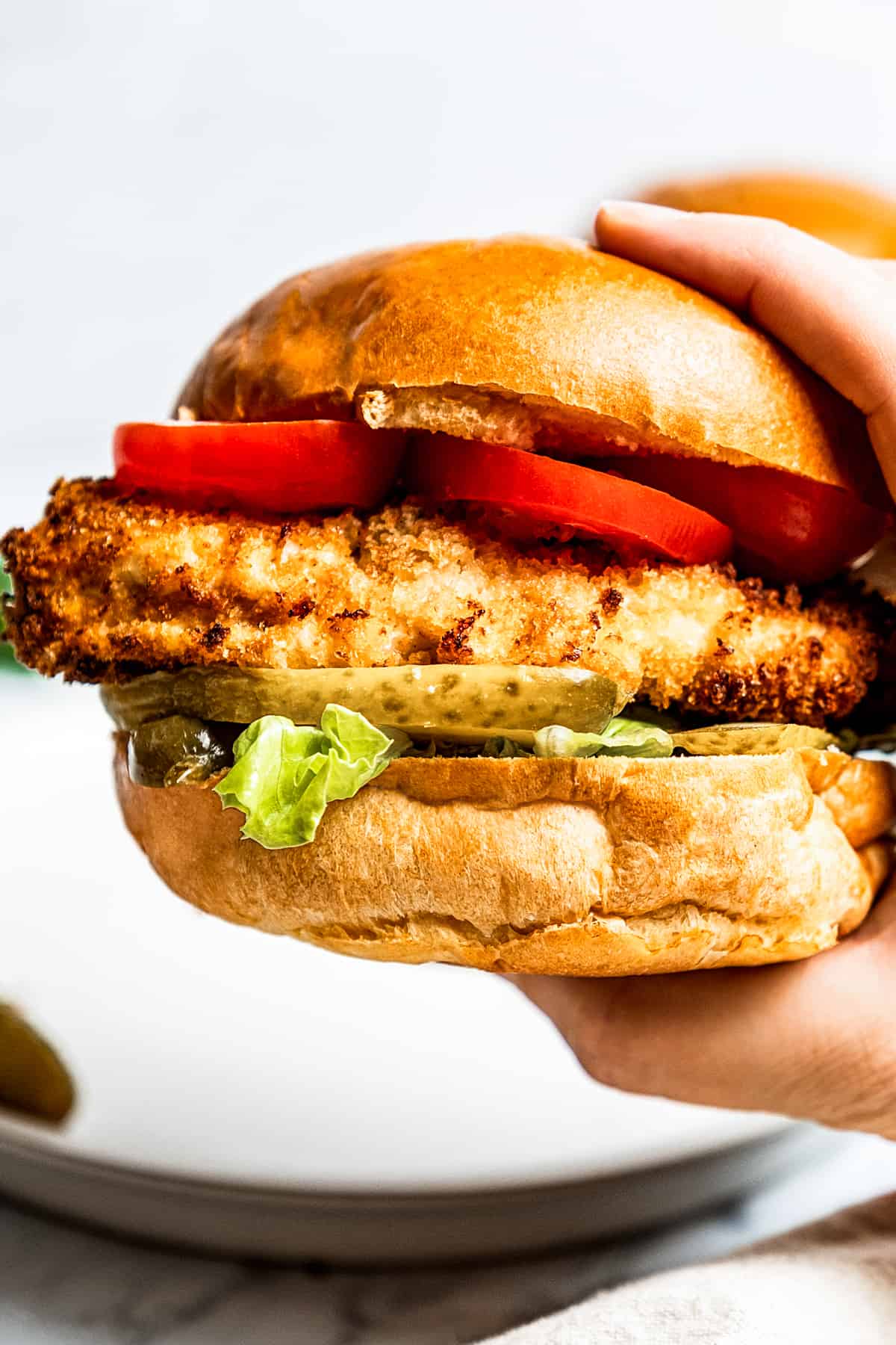 Holding a chicken sandwich toward the camera to show the air fryer chicken and toppings on a buttery bun.