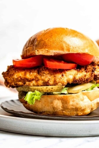 A fried chicken sandwich on a bun with lettuce, tomato, and pickles.
