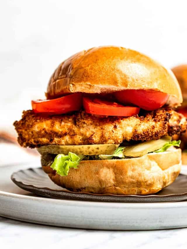 A fried chicken sandwich on a bun with lettuce, tomato, and pickles.