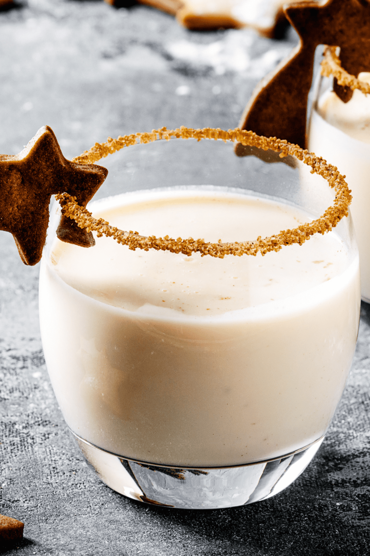 Eggnog in a glass with cinnamon, served in two glasses with star shape sugar cookies, fir branch over gray background.