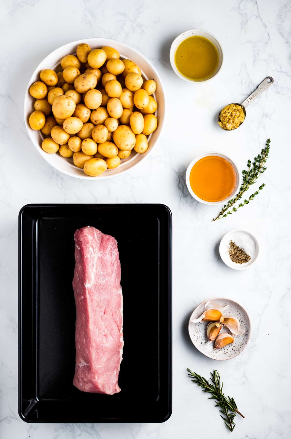 ingredients for honey garlic pork tenderloin: raw pork tenderloin, yellow potatoes, honey, garlic, butter, thyme leaves, salt, and pepper.